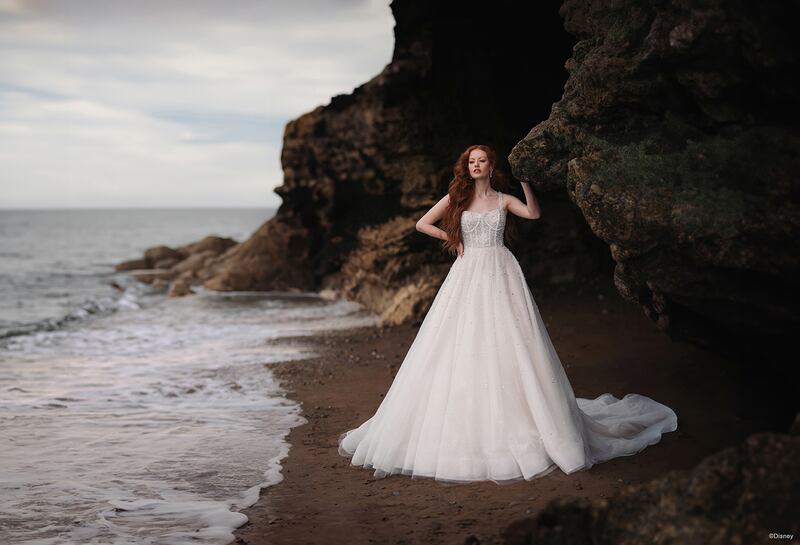 Realizado con el efecto translúcido de las espumosas burbujas oceánicas, cuentas perladas y un sutil brillo danzan sobre el corpiño de nuestro vestido Ariel Platinum de Disney, aportando brillo y vitalidad a los tonos champán y marfil del vestido de gala de tul con lentejuelas.